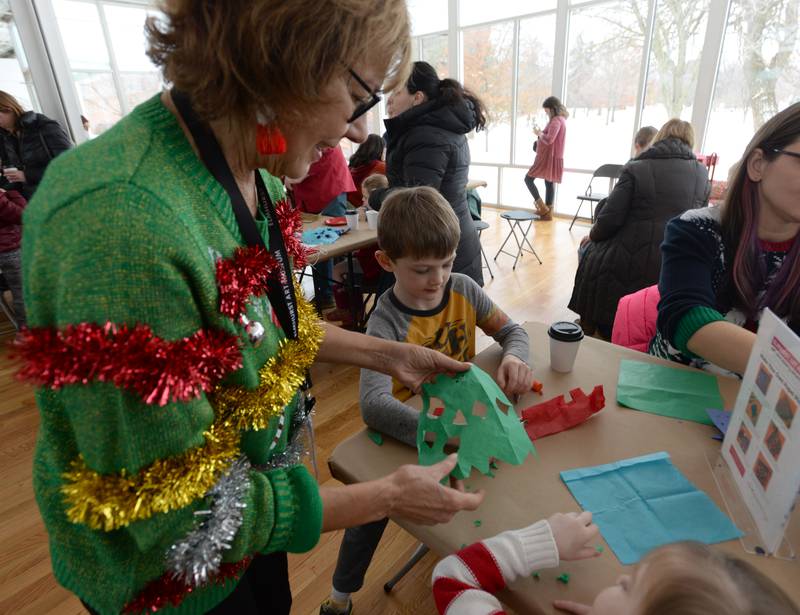 Elmhurst Art Museum volunteer Annette Armstrong helps children Peter Giovanetto of Elmhurst make snowflakes during the Family Holiday Party Saturday Dec 17, 2022.