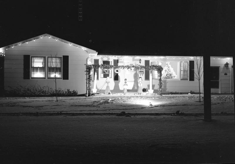 1108 S First Street in DeKalb in December 1965, the winner of the South Side Christmas Home Display Contest Honor Award two years in a row, for 1964 and 1965. The display included three carolers with lights and evergreens, large candlesticks, letters spelling out NOEL, and a white Christmas Tree in the picture window. They enhanced their theme with recorded Christmas music.