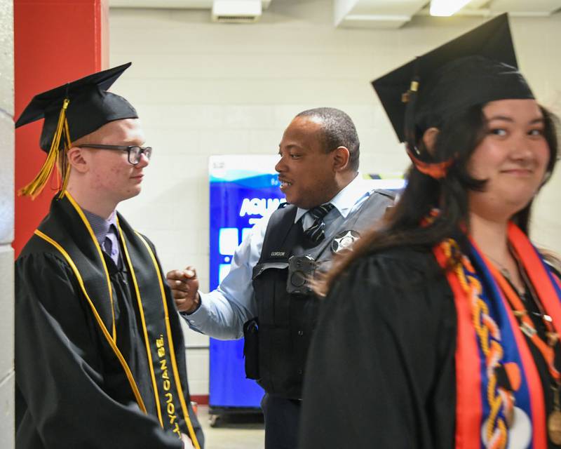 DeKalb High School resource officer fist bumps graduates as they make their way to the 2024 DeKalb High School commencement ceremony on Saturday, May 25, 2024, at the Northern Illinois University Convocation Center in DeKalb.