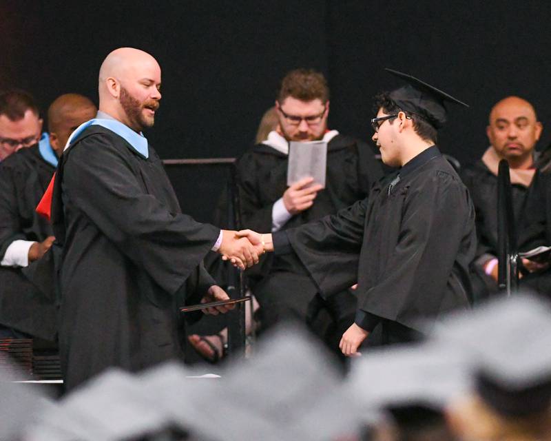 DeKalb High School senior Brandon Flores (right) receives congratulations from District 428 school board member Steve Byers as he gets his diploma during the 2024 DeKalb High School commencement ceremony on Saturday, May 25, 2024, at the Northern Illinois University Convocation Center in DeKalb.