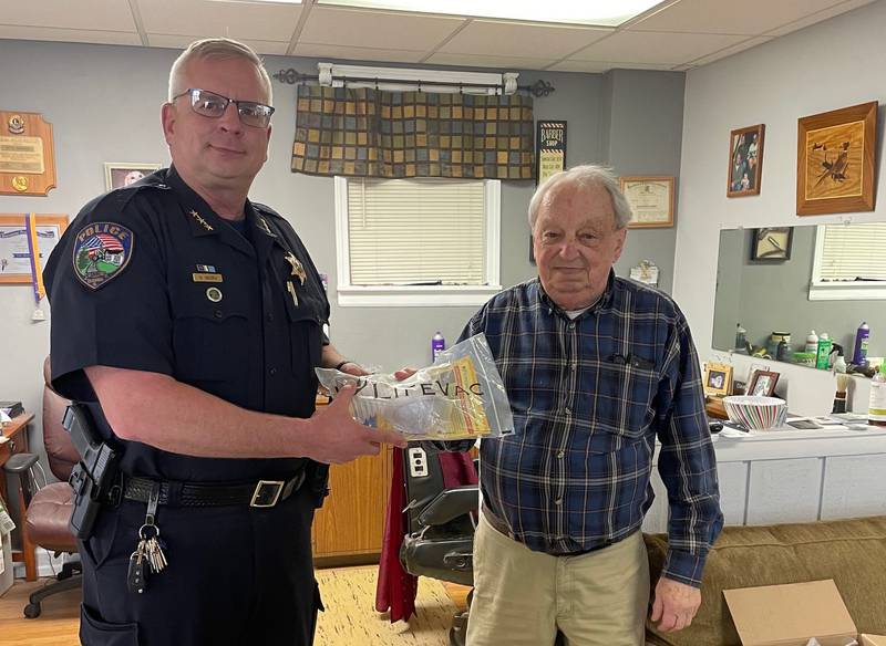 Elburn Police Chief Nick Sikora accepts from Dave Rissman (right), owner of Dave's Barber Shop in Elburn, a donation of eight Life Vac devices, one for each patrol car. Rissman and his son, Greg Rissman, together made the donation to the police. Greg owns Rissman Tax Service.