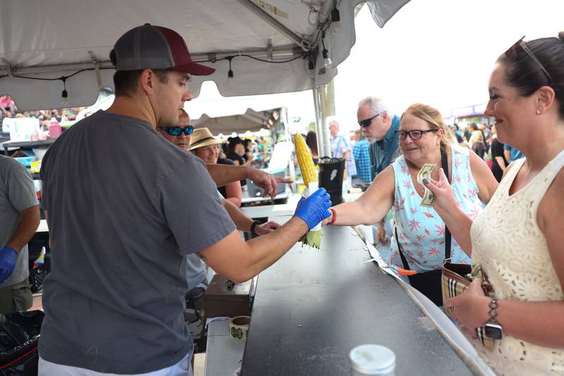 Joliet Firefighter Alex Garcia of Station 6 hands out a corn on the cob to Theresa Maice at the Firefighter Corn tent at the Taste of Joliet on Saturday, June 22, 2024 at Joliet Memorial Stadium.