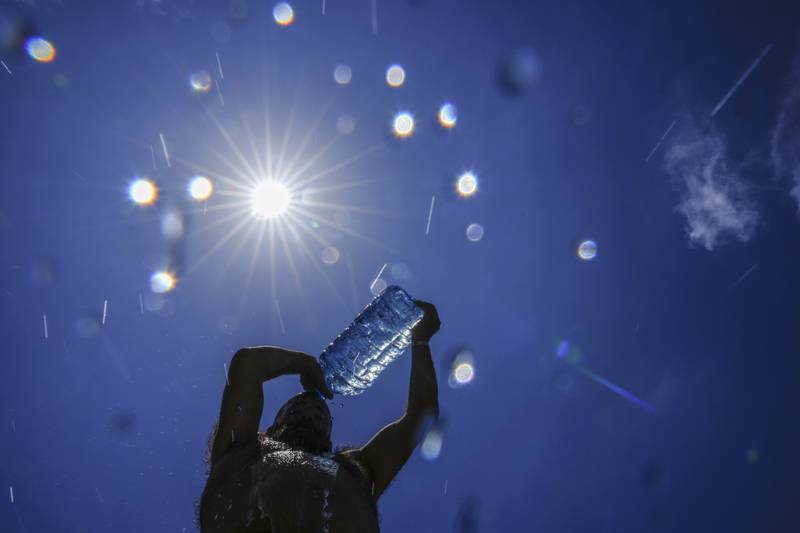 FILE - A man pours cold water onto his head to cool off on a sweltering hot day in the Mediterranean Sea in Beirut, Lebanon, Sunday, July 16, 2023. In the past 30 days, nearly 5,000 heat and rainfall records have been broken or tied in the United States and more than 10,000 records set globally, according to the National Oceanic and Atmospheric Administration. Since 2000, the U.S. is setting about twice as many heat records as cold. (AP Photo/Hassan Ammar, File)