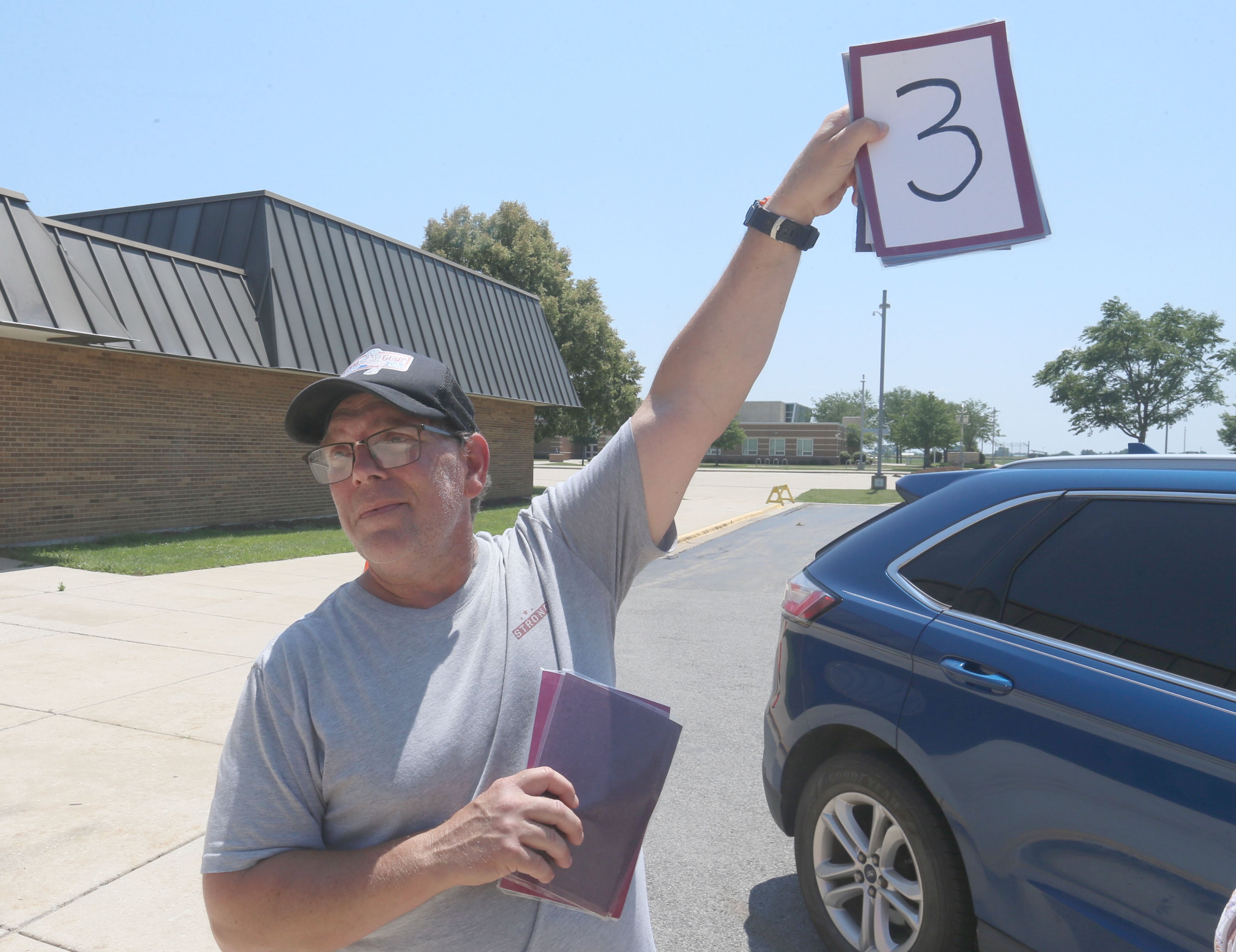 Chris Campbell takes food orders while holding up the number three outside of Sheppard Middle School on Wednesday, July 17, 2024 in Ottawa. The Summer Meal program provides two meals per day. The program is held every Wednesday from 10a.m.-1p.m. at the school. You must order the meal bags by clicking on the links posted on the Shepard Middle School Facebook page.