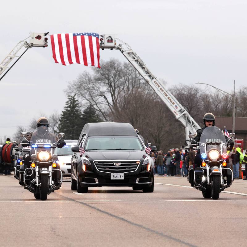 The hearse carrying the body of DeKalb County Sheriff’s Deputy Christina Musil goes under ladder trucks from the DeKalb and Shabbona Fire Departments Monday, April 1, 2024, on DeKalb Avenue in Sycamore during a processional to honor the fallen officer. Musil, 35, was killed Thursday while on duty after a truck rear-ended her police vehicle in Waterman.