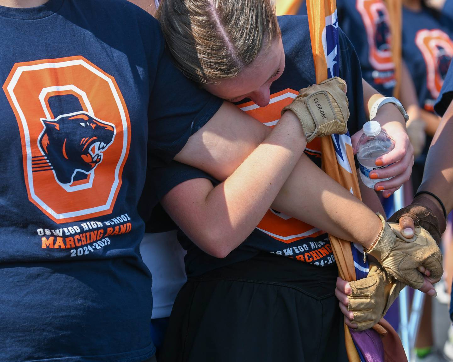 Oswego High School color guard members get comforted as the band plays Amazing Grace on Sunday Sept. 15, 2024, before the start of the homecoming parade to honor a classmate who passed away in a car crash.