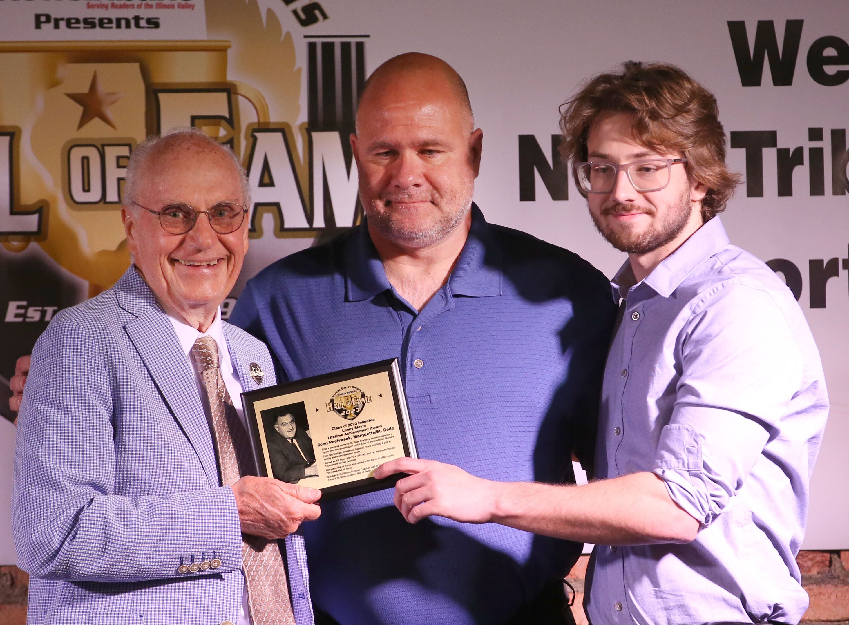 Tom and Jacob Pocivasek accept the Lanny Slevin Lifetime Achievement Award from Lanny Slevin Emcee, on behalf of their father John Pocivasek during the Shaw Media Illinois Valley Sports Hall of Fame on Thursday, June 8, 2023 at the Auditorium Ballroom in La Salle. John Pocivasek, had a star prep career at St. Bede Academy and was a legendary figure who was a multi-sport coach and athletic director at Marquette Academy for 38 years. 