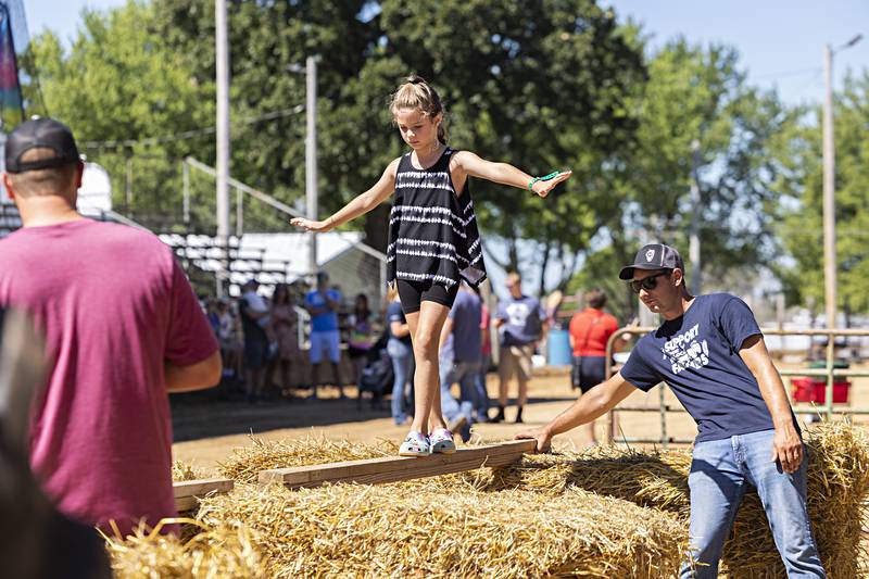 Whitley Iben, 6, of Thomson balances herself Saturday, August 12, 2023 between two hay bales during the Carroll County Fair’s Ninja Farmer obstacle course.