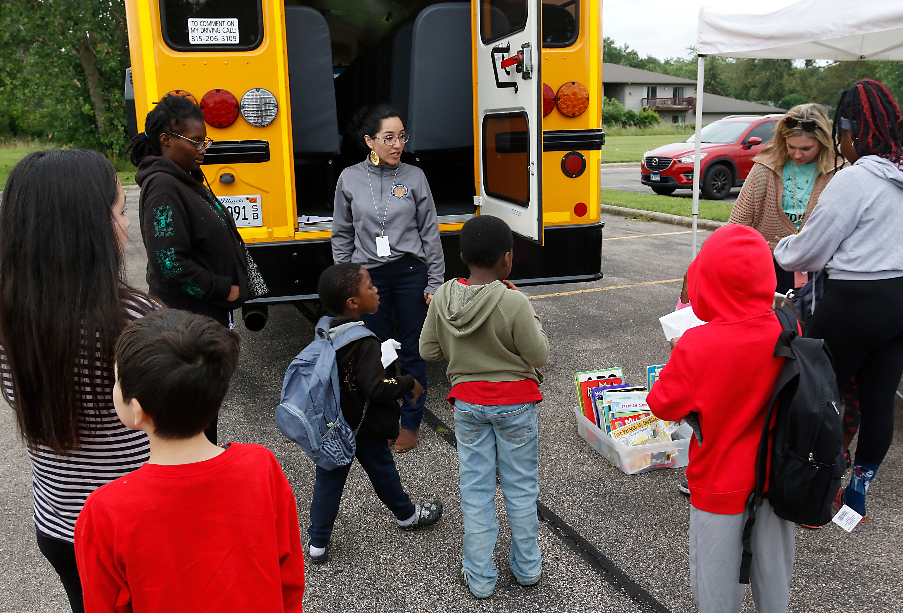 Gabi Ordonez talks with parents and students while handing out backpacks during a Woodstock School District 200 Back to School Coming to You event at Sheila Street Apartments on Tuesday, Aug. 6, 2024. The location was one of twelve stops on the tour that gave out backpacks and school supplies, provided registration help and computer repair.