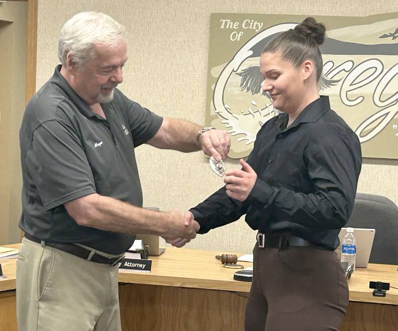 Oregon Mayor Ken Williams (left) hands Taylor Buckwalter her badge after swearing her in as the city's new patrol officer at the city council meeting on Tuesday, Aug. 27. 2024.