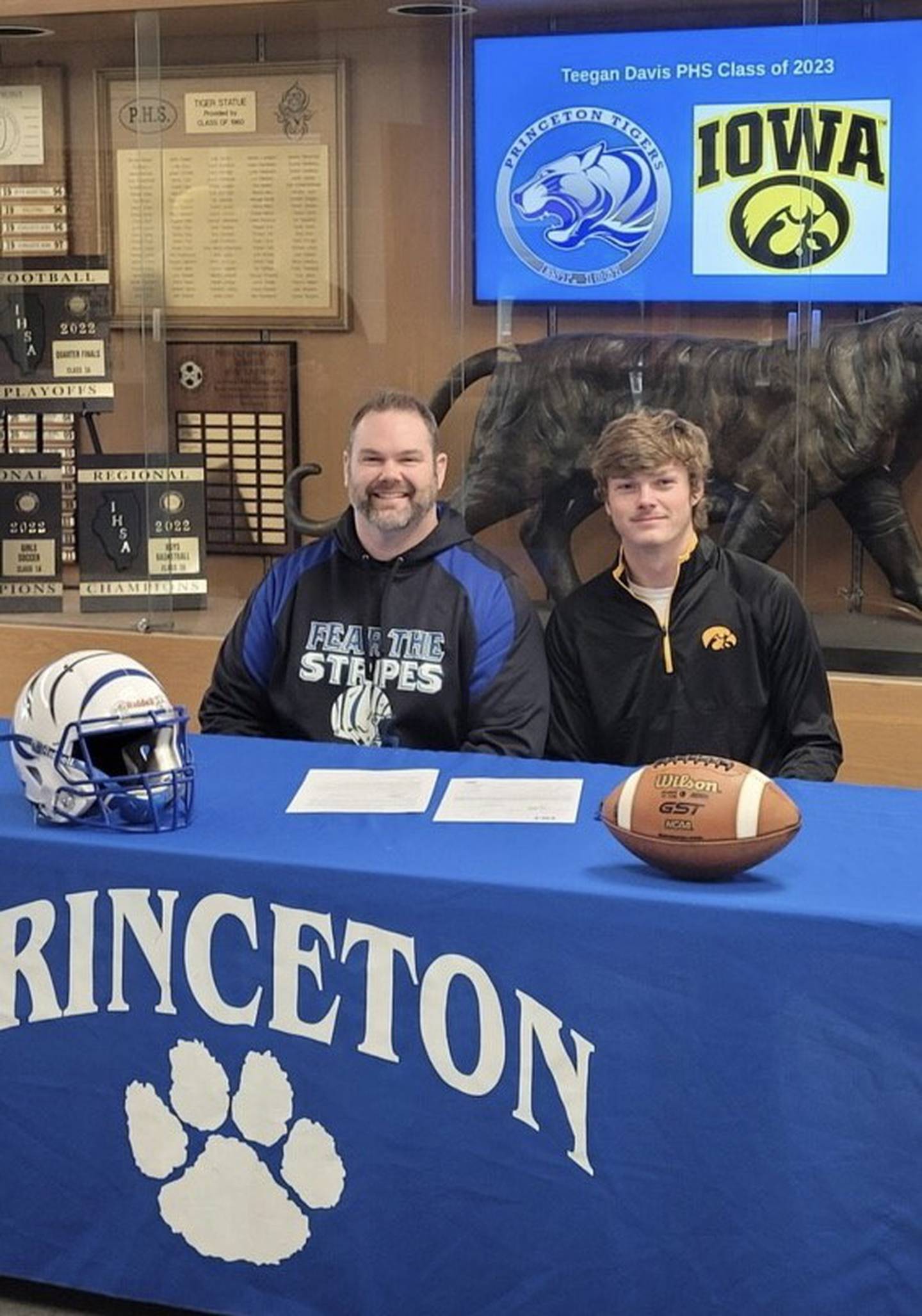 Princeton High School football head coach Ryan Pearson sits with PHS senior Teegan Davis after signing his National Letter of Intent to play football for the University of Iowa.