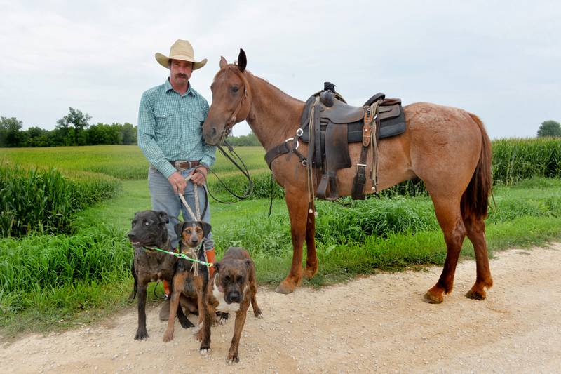 Wesley Bush stands with his one of his horses, Willy, and three of his dogs Hank, Collar, and Lizzy, near his home on Capp Road, northeast of Morrison. Bush is the owner/operator of 2B Cattle Catching Services.