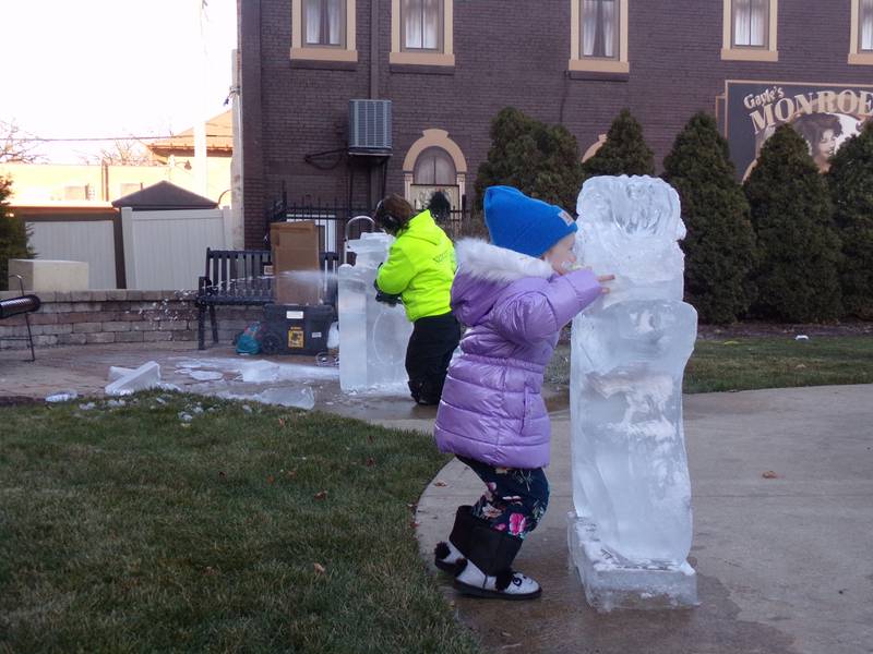 A little girl poses for a photo with one of the ice sculptures Saturday, Nov. 25, 2023, at Heritage Park in Streator during the Keeping Christmas Close to Home celebration.