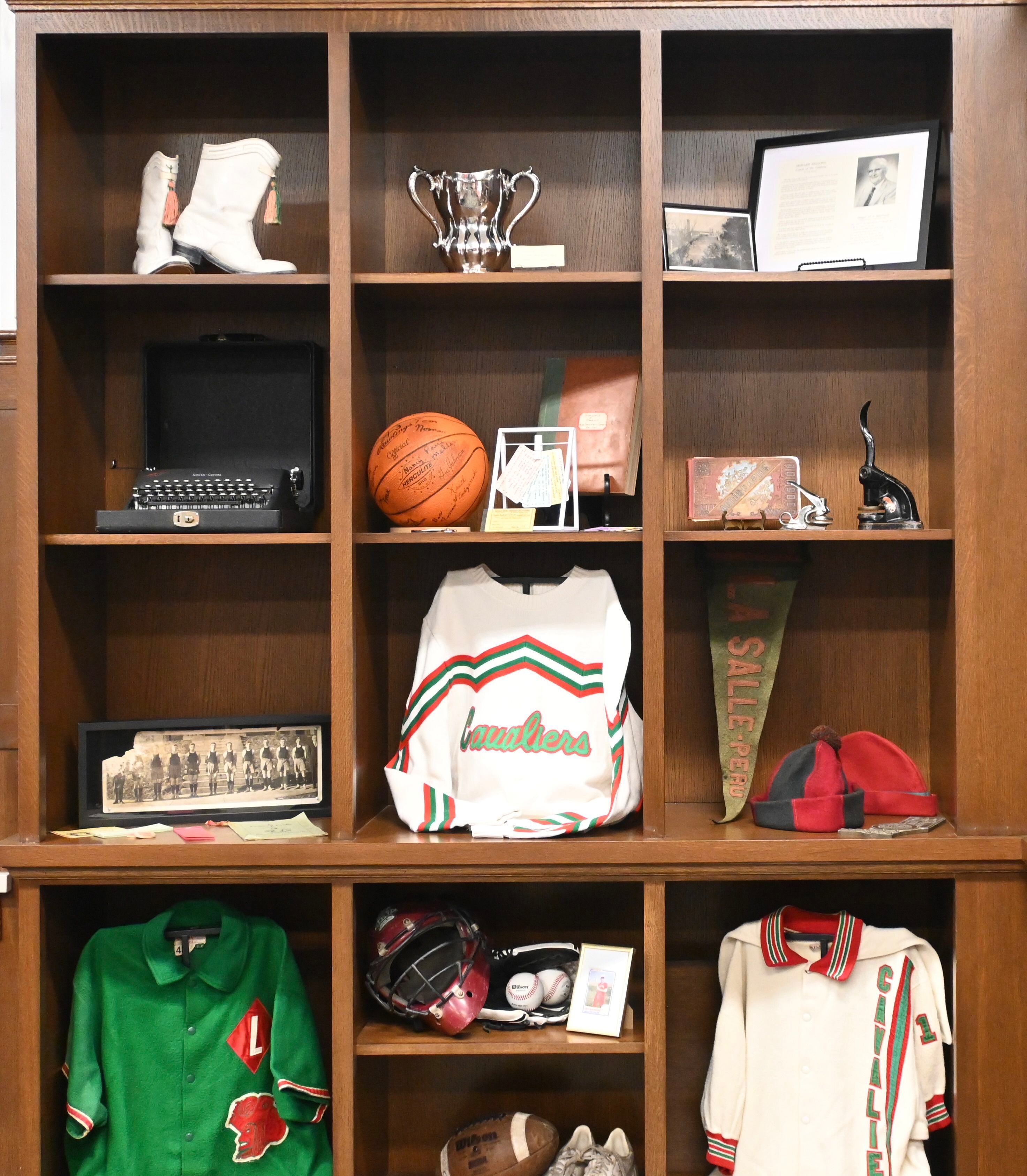 Custom wooden cabinets displaying artifacts throughout LP’s history such as a typewriter, yearbooks, and jerseys in the Herbolsheimer Alumni Room at La Salle Peru High School.