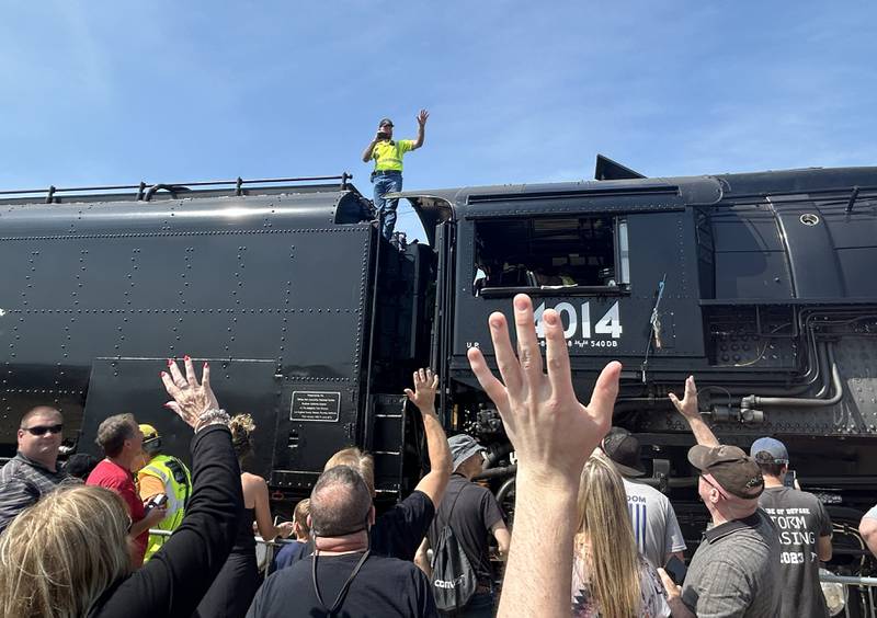 Ed Pickens, manager of the "UP steam team" for Big Boy 4014, stands on the massive steam locomotive and waves to the crowd as he films on Sunday, Sept. 8, 2024 during the daylong, free event in Rochelle.