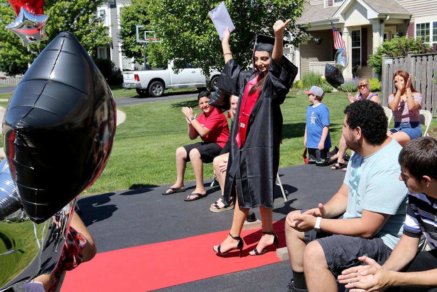 Julianna Ghanayem, 18, throws her arms up in celebration of receiving her Huntley High School diploma on Monday in Huntley. Principal Marcus Belin and other faculty members drove to graduating seniors' houses to personally deliver diplomas with a socially distant ceremony with "Pomp and Circumstance" bellowing from the bus.