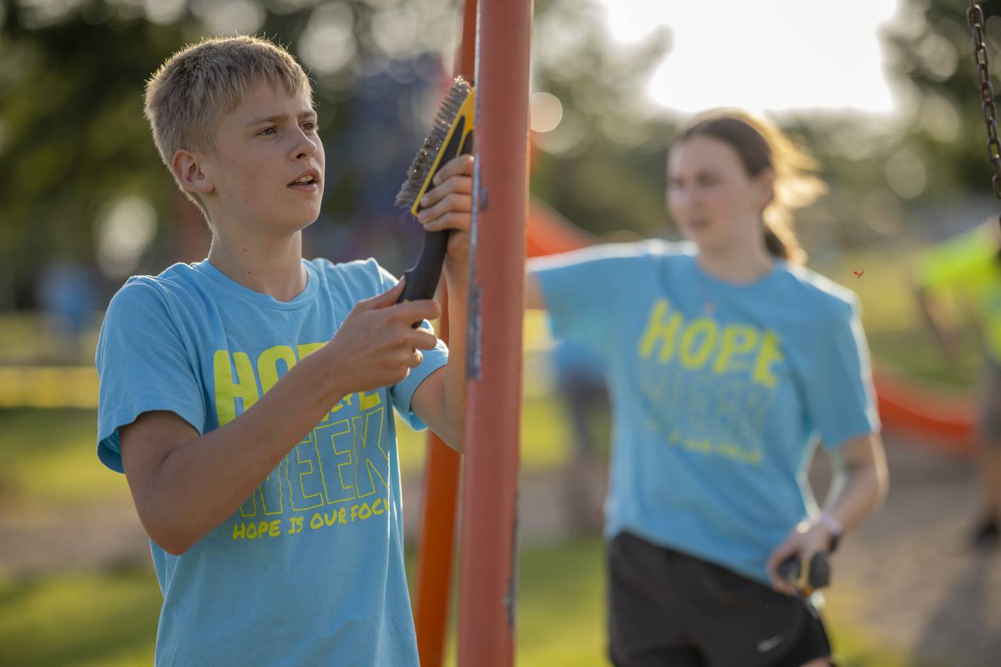 Owen McConville (left) and Sadie Kiersnowski (right) scrape chipped old paint off of the swing set in preparation for fresh paint at Tonica New Park on June 3, 2024.