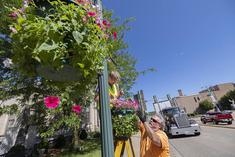 City employees James Leslie (left) and John Sheridan work to decorate Galena Avenue on Wednesday, May 29, 2024, with petunia baskets. Dixon in Bloom, the organization responsible for the pink flowers, has prepared 306 baskets for the town.