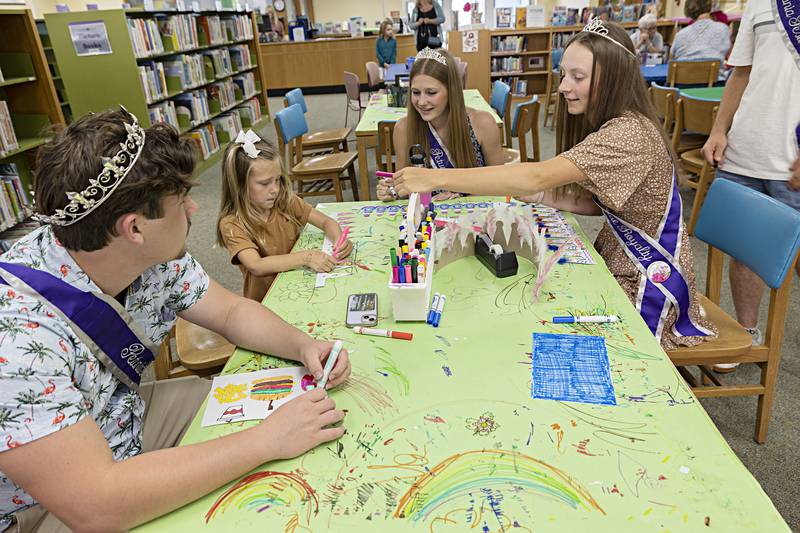 Surrounded by Petunia royalty Ellia Pearson, 5, gets help and encouragement Wednesday, June 28, 2023 by male attendant Logan Devine, Queen Teyla Wendt and female attendant Katie Drew as she works on a craft at the Dixon library. The royalty spend the afternoon at the library helping make crowns and other art pieces with young visitors.
