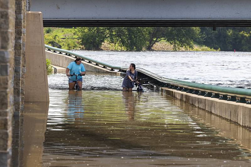 Ayla and Charlie Arellano wade through high waters Monday, July 15, 2024, below the Peoria Avenue bridge as river levels continue to raise as more rains hit the area.