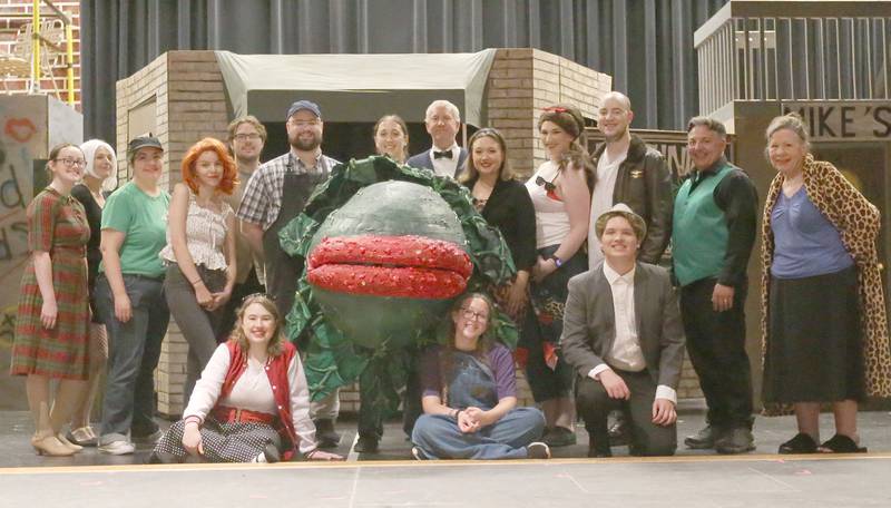 The cast of the Little Shop of Horrors pose for a photo on Monday, June 17, 2024 at Mendota High School. Members are  back row standing from left to right: Abby Siri, ensemble; Melissa Clark, ensemble; Jacqui Margowski, ensemble; Mia Raya, Crystal; Matthew Grenter, ensemble; Austin Allbert, Seymour; Abby Hesslau, plant puppeteer; the third of four Audrey IIs (plants); Kevin Wohrley, Mr. Mushnik; Haleigh Zorn, Audrey; Madeline Enervold, Ronnette; Cole Enervold, Orin Scrivello D.D.S.; Mike Anderson, voice of Audrey II (the plant); Linda Whitmore, ensemble - front row seated / kneeling from left to right: Jillian Younger, Chiffon; Brianna Russell, stage crew; Trekker Klema, ensemble.