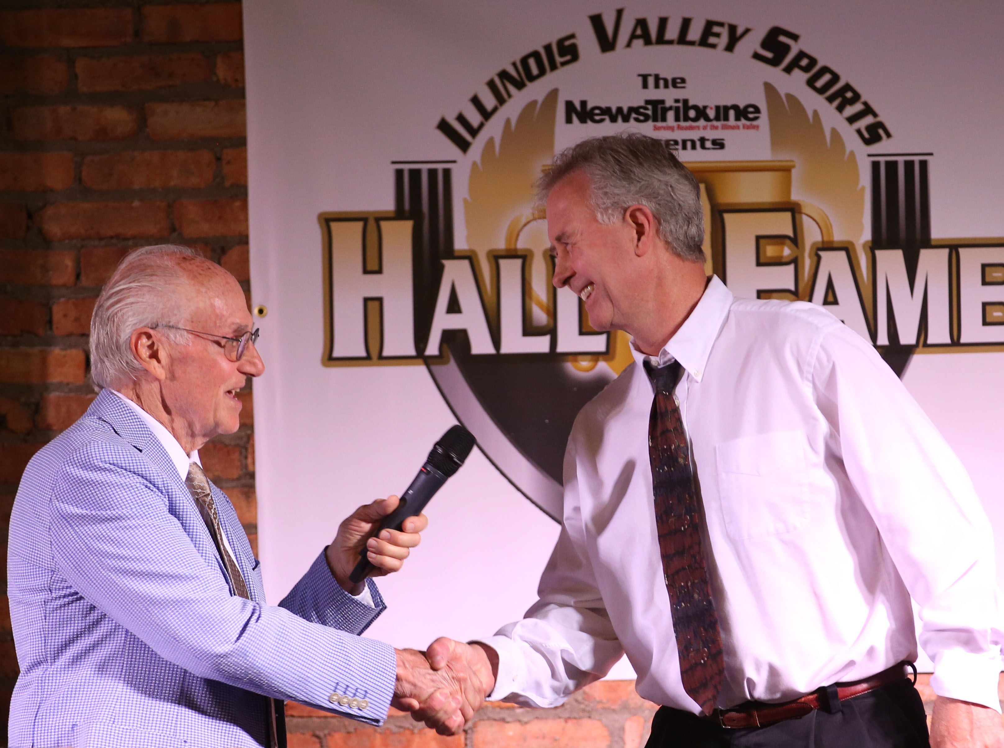 Lanny Slevin Emcee, congratulates Tom Henderson Jr. as he accepts the award of his father Tom henderson Sr. during the Shaw Media Illinois Valley Sports Hall of Fame on Thursday, June 8, 2023 at the Auditorium Ballroom in La Salle. Henderson was the boys and girls tennis coach at Ottawa Township High School from 1958-2007. 