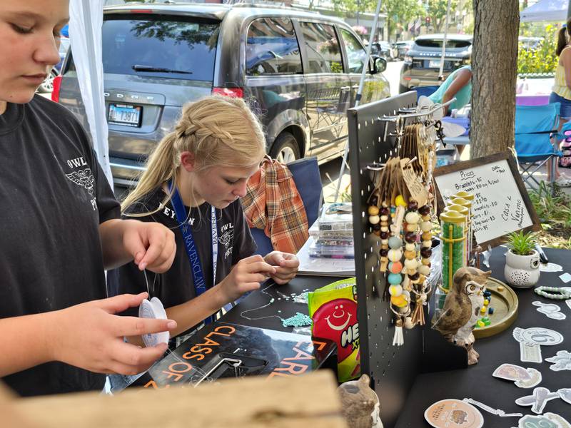 Sophia Sly (left) and Peyton Woods make a custom made bracelet at their business Owl Post on Saturday, Aug. 24, 2024, during the third annual Prairie Fox Books Children's Business Fair in downtown Ottawa.