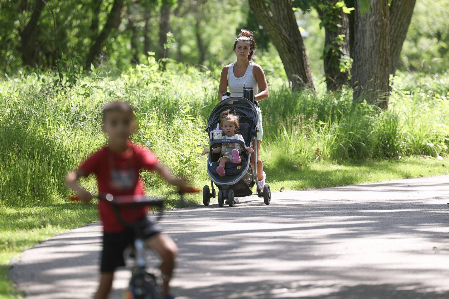 Lexi Gordon pushes her daughter Gia while her son Vinny rides his bike along a trail at the Forest Preserve District of Will County Rock Run Preserve on Thursday June 6, 2024 in Joliet.