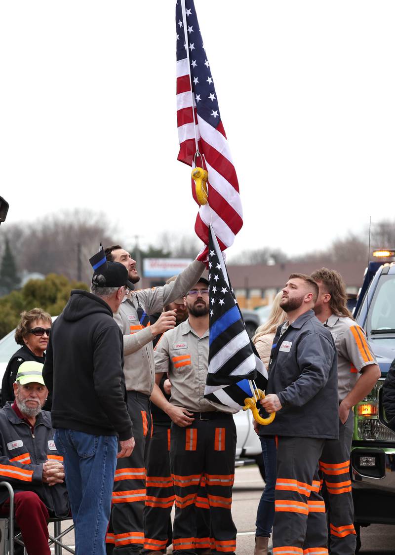 Workers from Lovetts Towing & Recovery raise flags on their crane over DeKalb Avenue in Sycamore Monday, April 1, 2024, before a processional honoring DeKalb County Sheriff’s Deputy Christina Musil. Musil, 35, was killed Thursday while on duty after a truck rear-ended her police vehicle in Waterman.