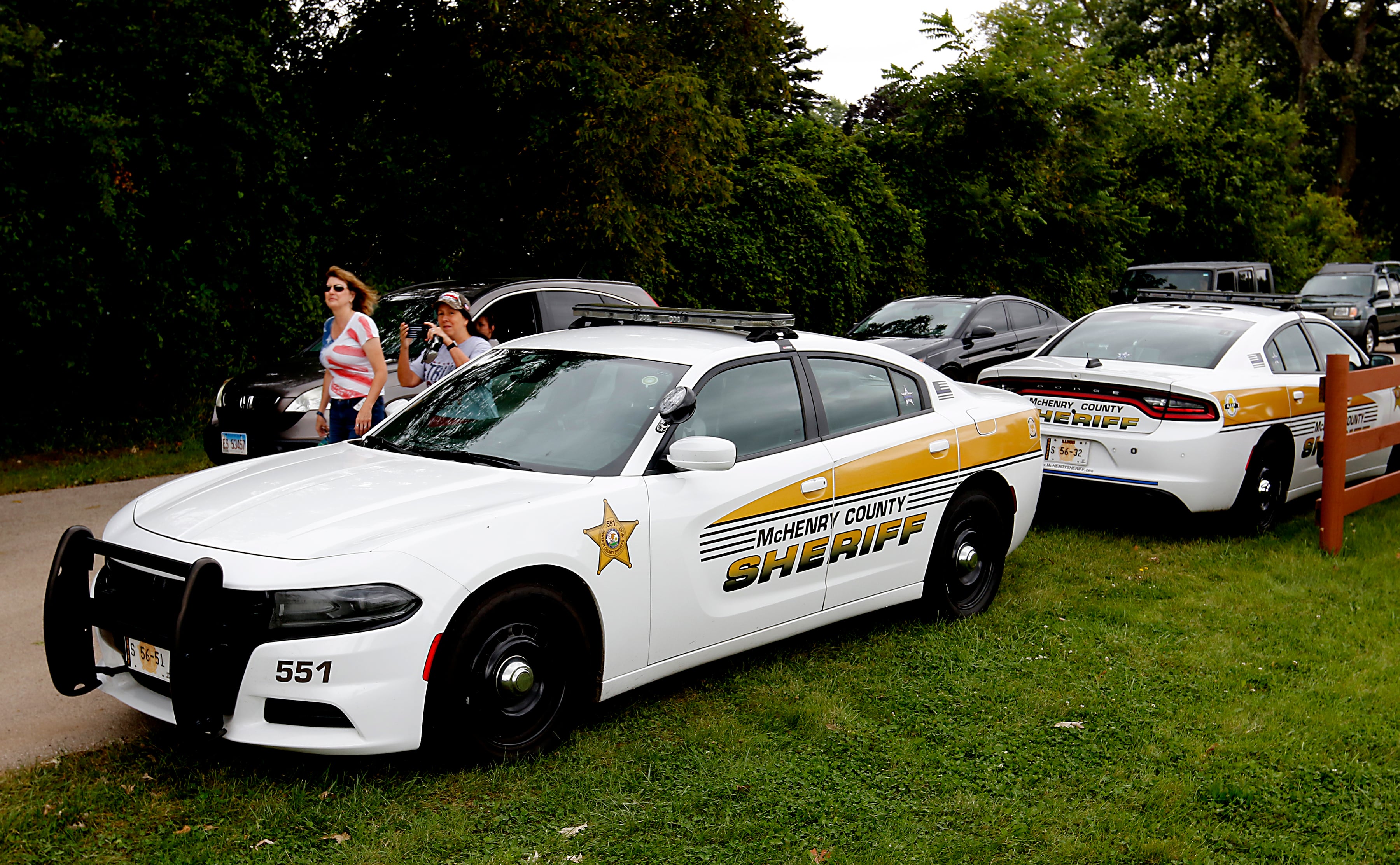 People walk and drive past police cars as they enter the McHenry County Fairgrounds for the Trump Now-Save the American Dream Rally on Sunday Aug. 18, 2024, in Woodstock.