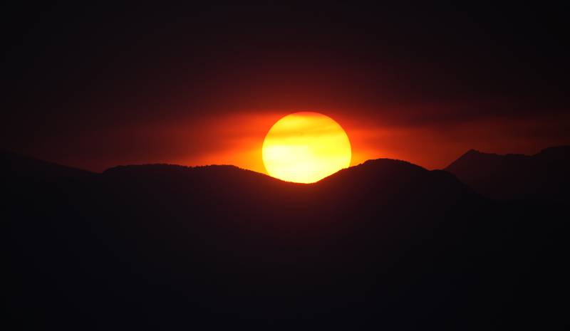 FILE - The suns sets behind the Rocky Mountains after daytime high temperatures reached above 90-degrees Fahrenheit, 32 Celsius, Monday, June 26, 2023, in Denver. As the heat breaks records, weakening and sickening people, it’s worth remembering that dire heat waves have inspired effective efforts to prevent heat illness.