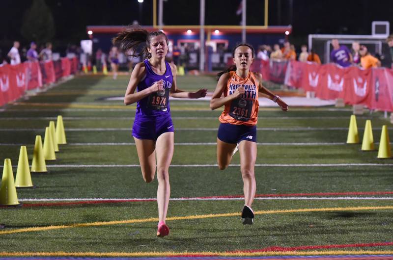 Downers Grove North’s Lily Eddington catches Naperville North’s Juie Piot at the finish line of the Naperville Twilight Cross Country meet at Naperville North High School on Wednesday night, October 4, 2023. They placed third and fourth.