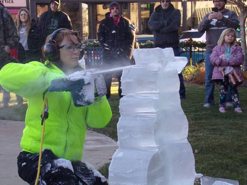 An ice sculptor creates a snowman out of a block of ice Saturday, Nov. 25, 2023, as spectators watch at Heritage Park in Streator during the Keeping Christmas Close to Home celebration.