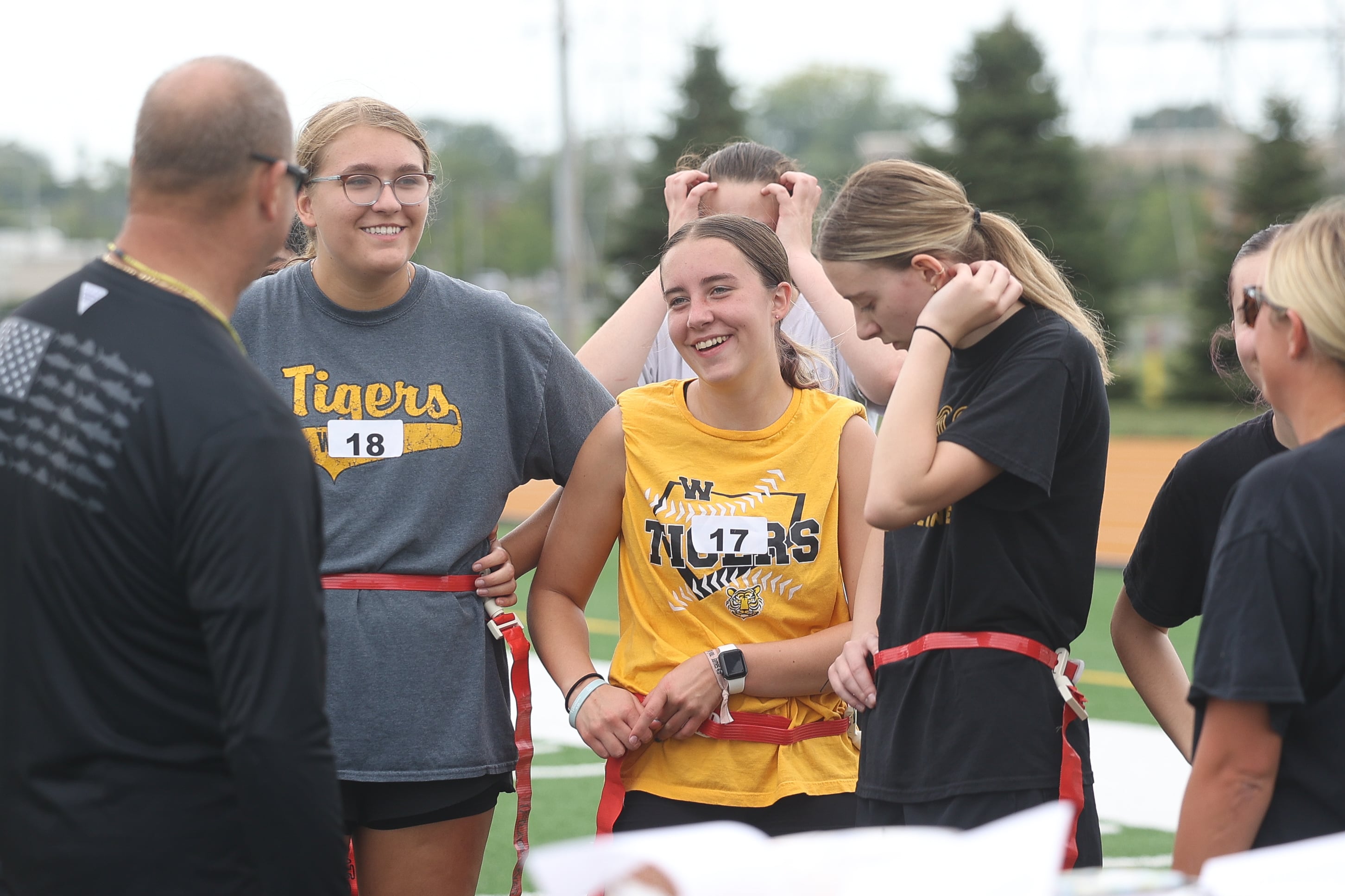 Georgie Nevermen, left, Taryn Faulhaber and Samantha Casanova have a laugh with the coach between drills at Joliet West’s girls flag football tryouts on Monday, Aug. 12, 2024 at Joliet West High School.