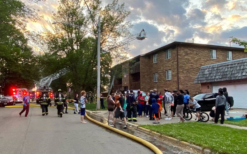 Neighbors and residents gather outside a corner at Kimberly Drive and Normal Road in front of a building while crews work to battle a structure fire at a Husky Ridge apartment complex in the 800 block of Kimberly Drive, DeKalb, on Wednesday evening, May 29, 2024.