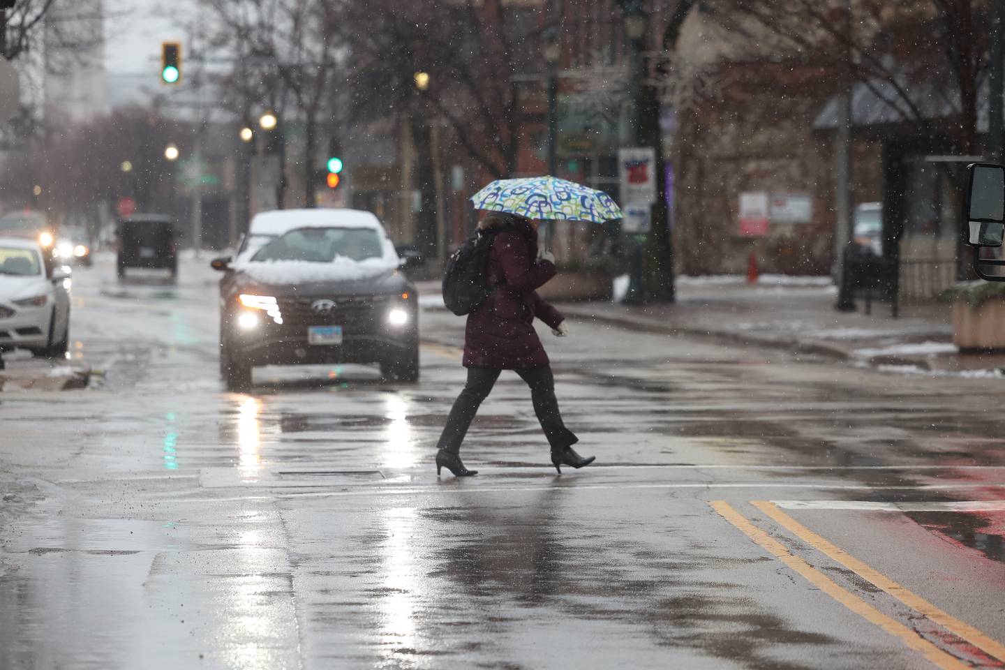 A pedestrian crosses the street with an umbrella in downtown Joliet as morning snow turned to afternoon rain on Tuesday, Jan. 9th, 2024.