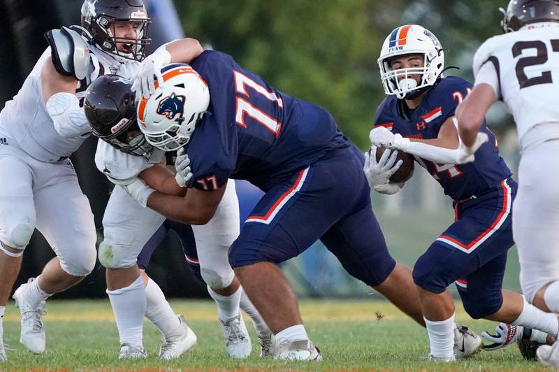 Oswego’s Benjamin McCollum (77) opens a hole for Ayden Villa (24) off a block against Joliet Catholic's Derrick Pomatto (46) during a football game at Oswego High School on Friday, Sep 6, 2024.