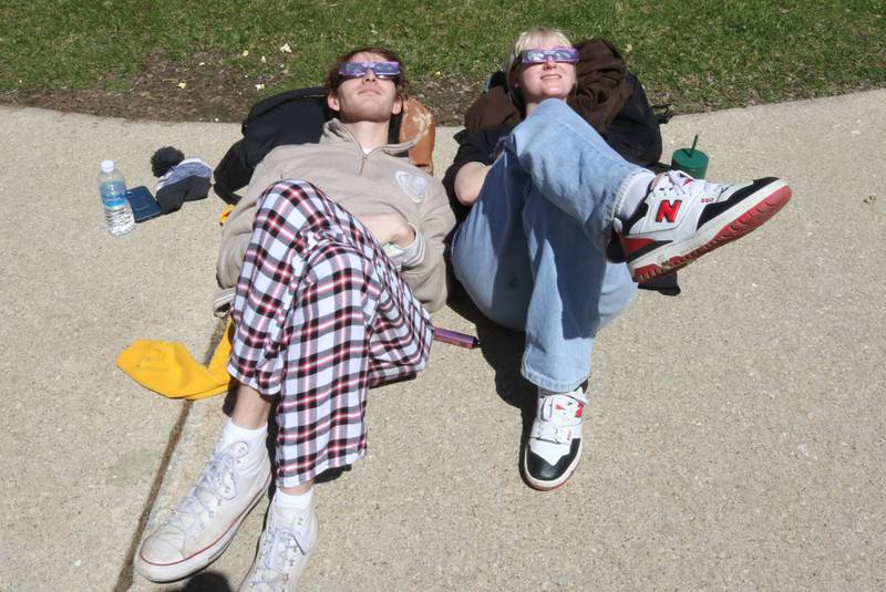 Benjamin Osborn, a Northern Illinois University senior from Rockford, and Emily Claussen, a senior, from McHenry, get comfortable to watch the eclipse progress Monday, April 8, 2024, during the NIU Solar Eclipse Viewing Party behind Davis Hall in DeKalb. Attendees were treated to perfect weather to watch the rare celestial event.