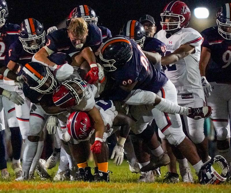 A number of Oswego defenders including Carson Cooney who lost his helmet in the play tackle West Aurora's Eliseo Liscano (1) during a football game at Oswego High School on Friday, Sept. 29, 2023.