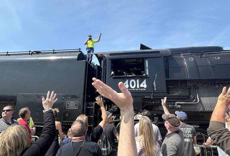 Ed Pickens, manager of the "UP steam team" for Big Boy 4014, stands on the massive steam locomotive and waves to the crowd as he films on Sunday, Sept. 8, 2024 during the daylong, free event in Rochelle.