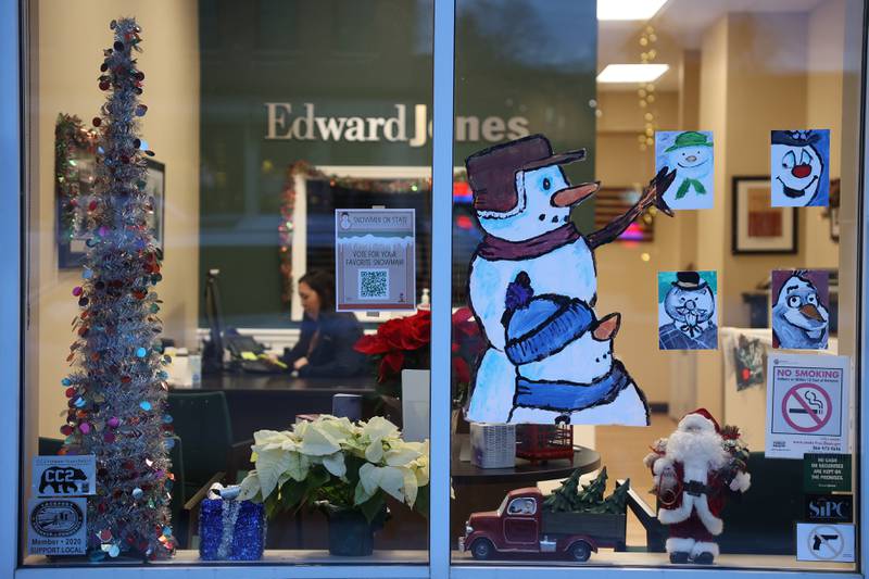 A snowman and son view portraits of famous snowmen in Edwards Jones Investments in downtown Lockport on Friday, Dec.15th, 2023. Snowmen decorate the windows of 25 store fronts in downtown Lockport for the holidays.