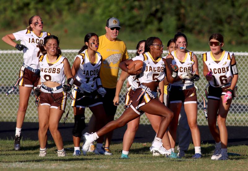 Jacobs’ players shout encouragement as Aaliyah Guichon hustles toward the end zone with a touchdown in varsity flag football on Tuesday, Sept. 3, 2024, at Dundee-Crown High School in Carpentersville.