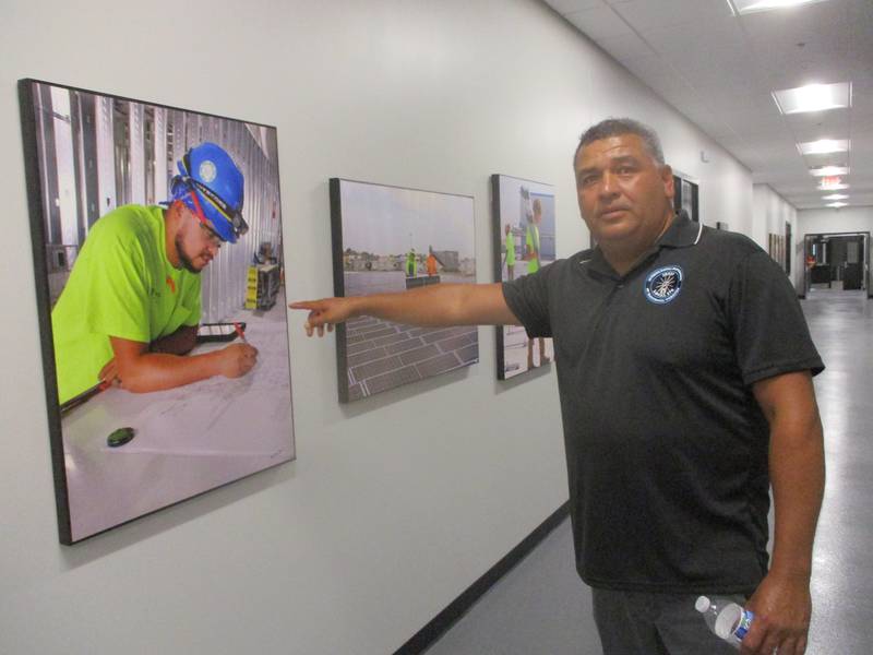 Juan Rico, assistant business agent for International Brotherhood of Electrical Workers Local 176, points to one of the many mounted photographs showing apprentices on the job at the Joliet Electrical Training Center. Sept. 12, 2024