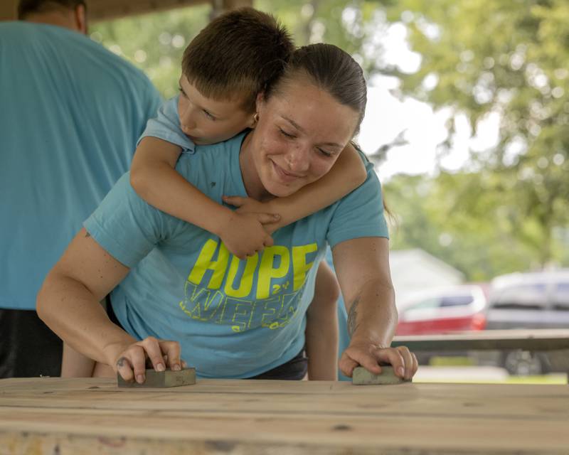Toni Presthus carries her son Colson as she sands picnic tables in preparation for new paint at Veteran's Park in Granville on June 4, 2024.
