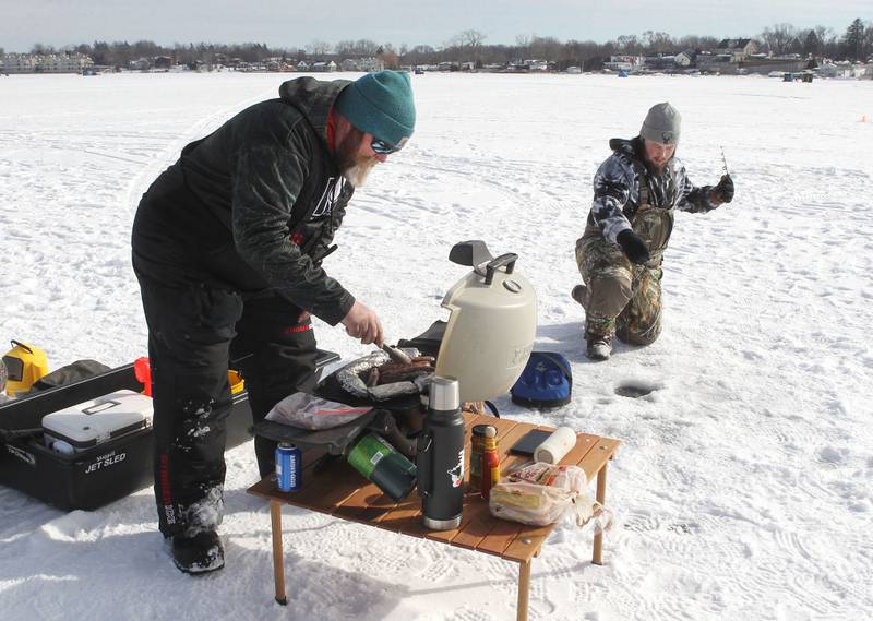 In this 2022 file photo, Grant Schmidt of Island Lake makes brats and venison tamales while his son, Cole, works on catching a fish during the LVVA Ice Fishing Derby on Bangs Lake in Wauconda. This year's derby takes place Jan. 26-28. More information can be found at www.waucondaicefishingderby.com.