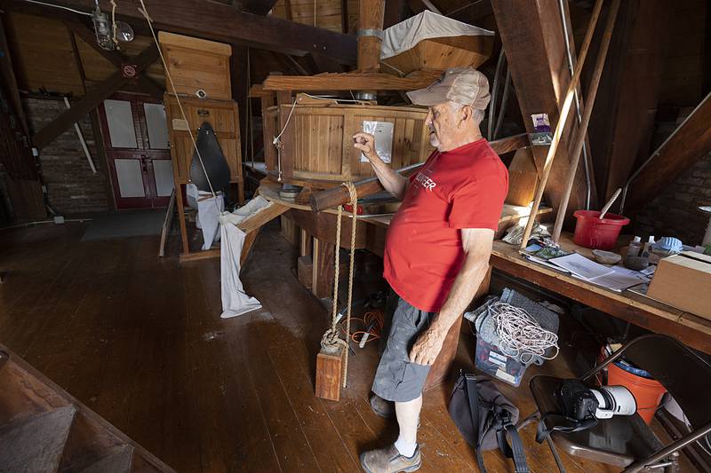 Russell gestures while talking about the lever that raises and lowers the grinding wheel Friday, June 7, 2024 at the Fulton windmill.