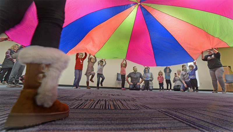 Children try to stand on one leg while raising a parachute . This was part of the Parachute Play program Friday at the Reddick Library in Ottawa.