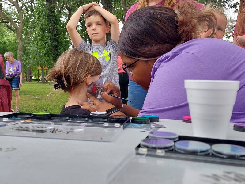 Kyli Rhines has her face painted by Sha'ron Teamer during Streator Unlimited's Fun Day on Tuesday, June 4, 2024, at City Park in Streator. Kyli's brother Brayden (behind) waits his turn to go next.