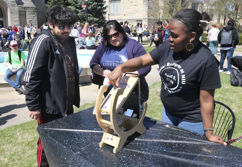 Alessandro Vargas, (left) a Northern Illinois University freshman from DeKalb, and Angie Vargas, from DeKalb, listen to Dorcas Joseph, (right) an NIU grad student from Nigeria, as she explains her Sunspotter eclipse viewer Monday, April 8, 2024, during the Northern Illinois University Solar Eclipse Viewing Party behind Davis Hall at NIU in DeKalb. Attendees were treated to perfect weather to watch the rare celestial event.