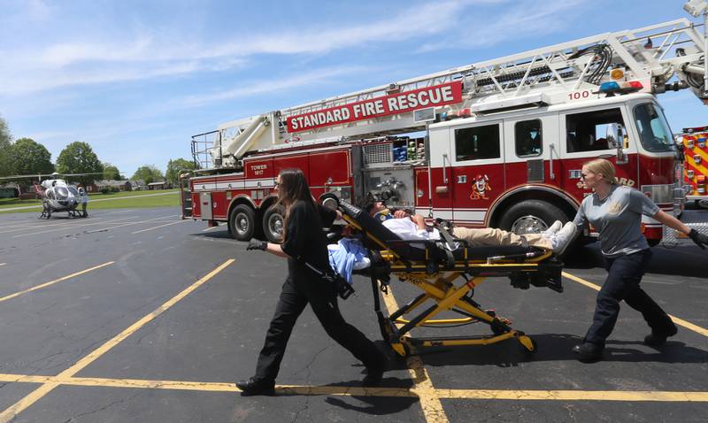 Putnam County EMS personnel Caitlyn Bradner and Jordan Mitchell wheel Putnam County High School student Rudy Villagomez on a stretcher during a "mock prom" scene through the Putnam County Corner's Awareness Program on Friday, May 3, 2024 at Putnam County High School.  Putnam County Fire and EMS units, PC Sheriff, and OSF Lifeflight crew conducted a drill crash scene. The school's prom is Saturday. The program helps students make good choices on prom night.